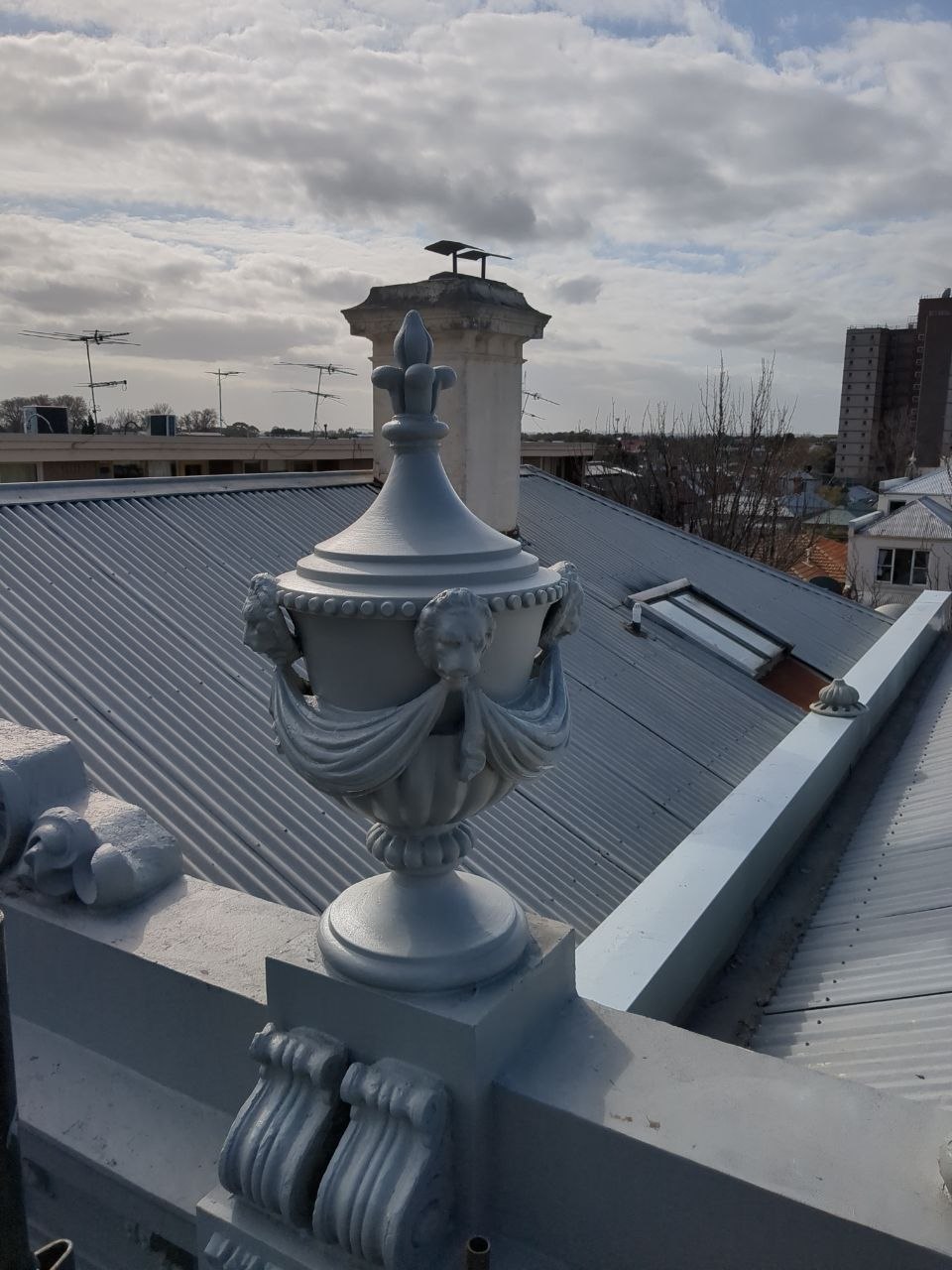 Restored urn finial reinstated on heritage parapet with rooftop view, Melbourne VIC