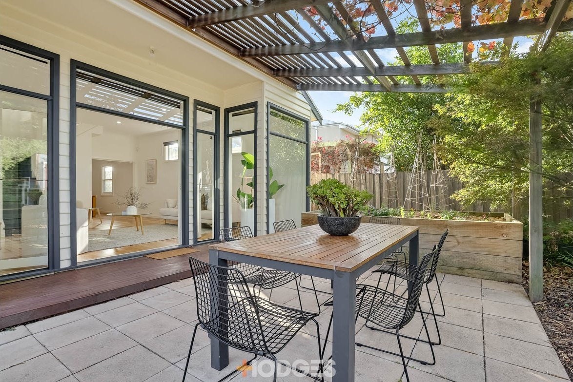Completed rear patio and pergola of a restored Newport weatherboard home with repainted window frames and glass doors