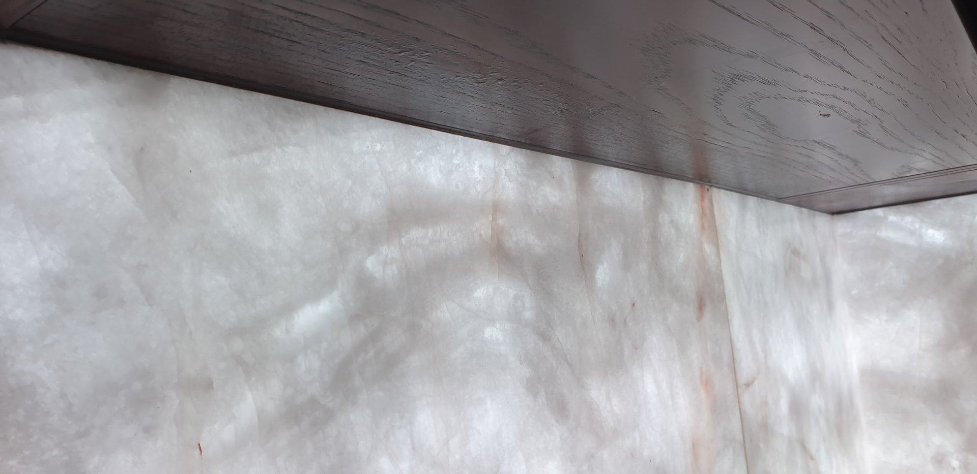 Close-up of a neatly sealed joint between a dark benchtop and a stone feature panel