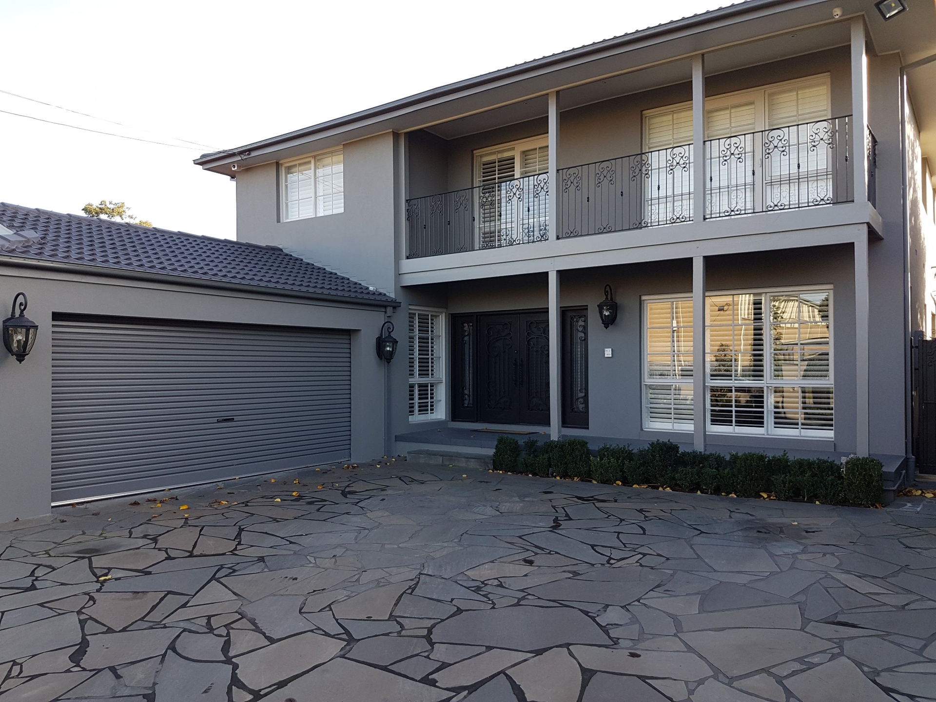 Grey rendered two-storey home with garage, stone driveway and decorative iron balcony, Melbourne VIC