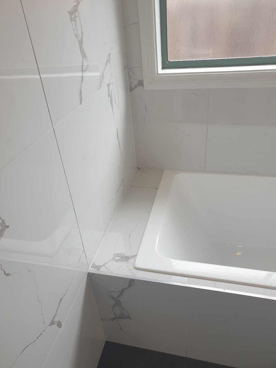 Bathtub set into marble-look tiled walls in the completed bathroom
