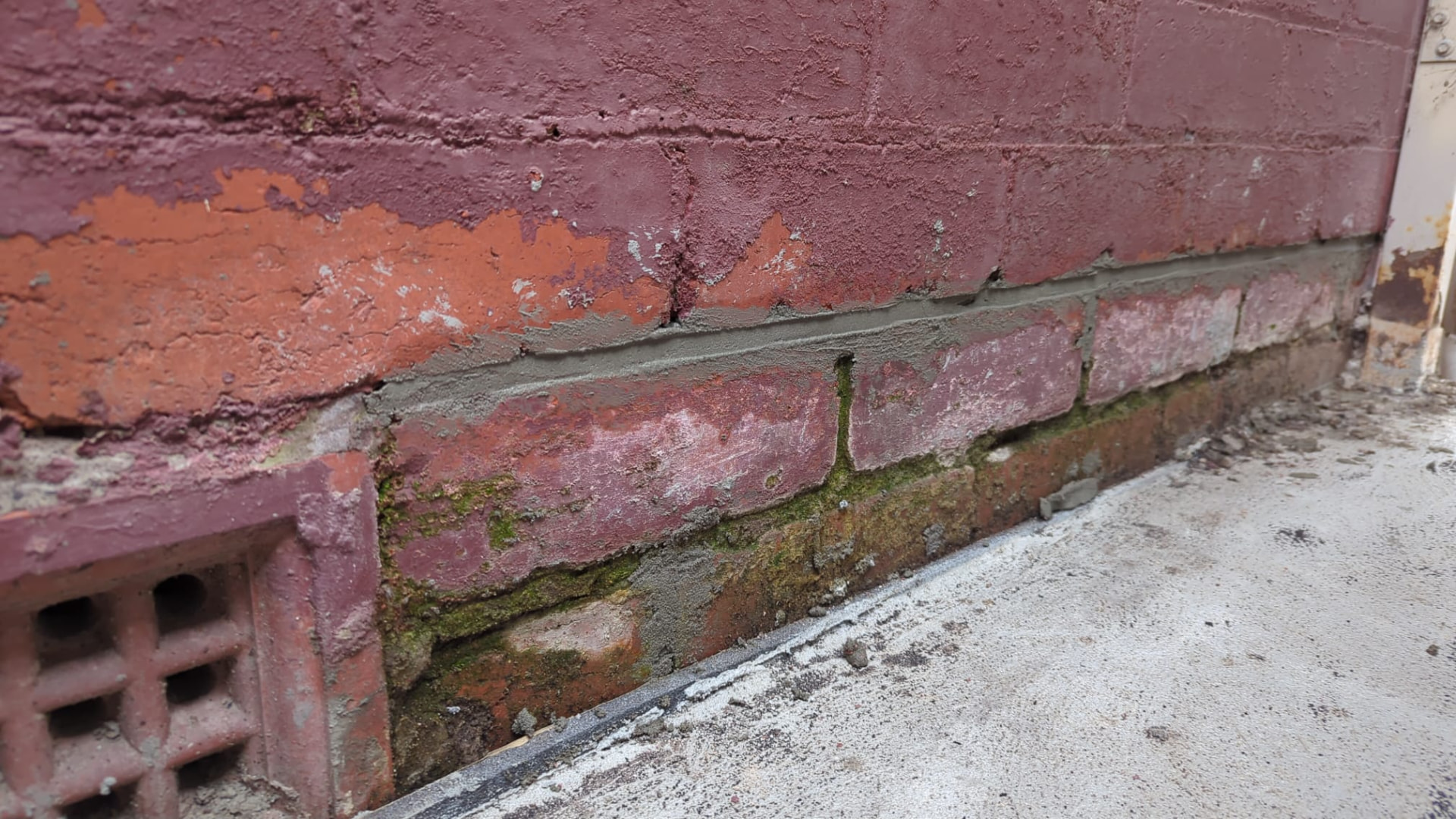 Wider view of brickwork and mortar condition showing weathered bricks, worn joints and moss at the base of the wall