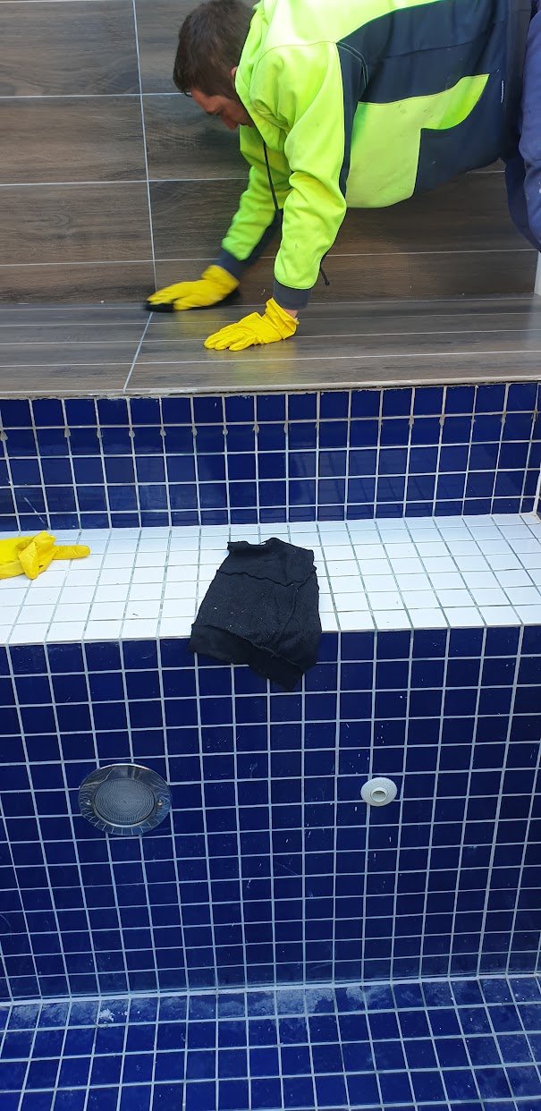 Applying grout to blue mosaic tiles during wet area maintenance work