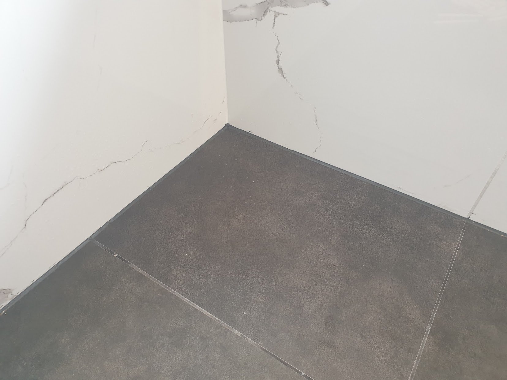 New dark floor tiles and marble-look wall tiles in the repaired shower area