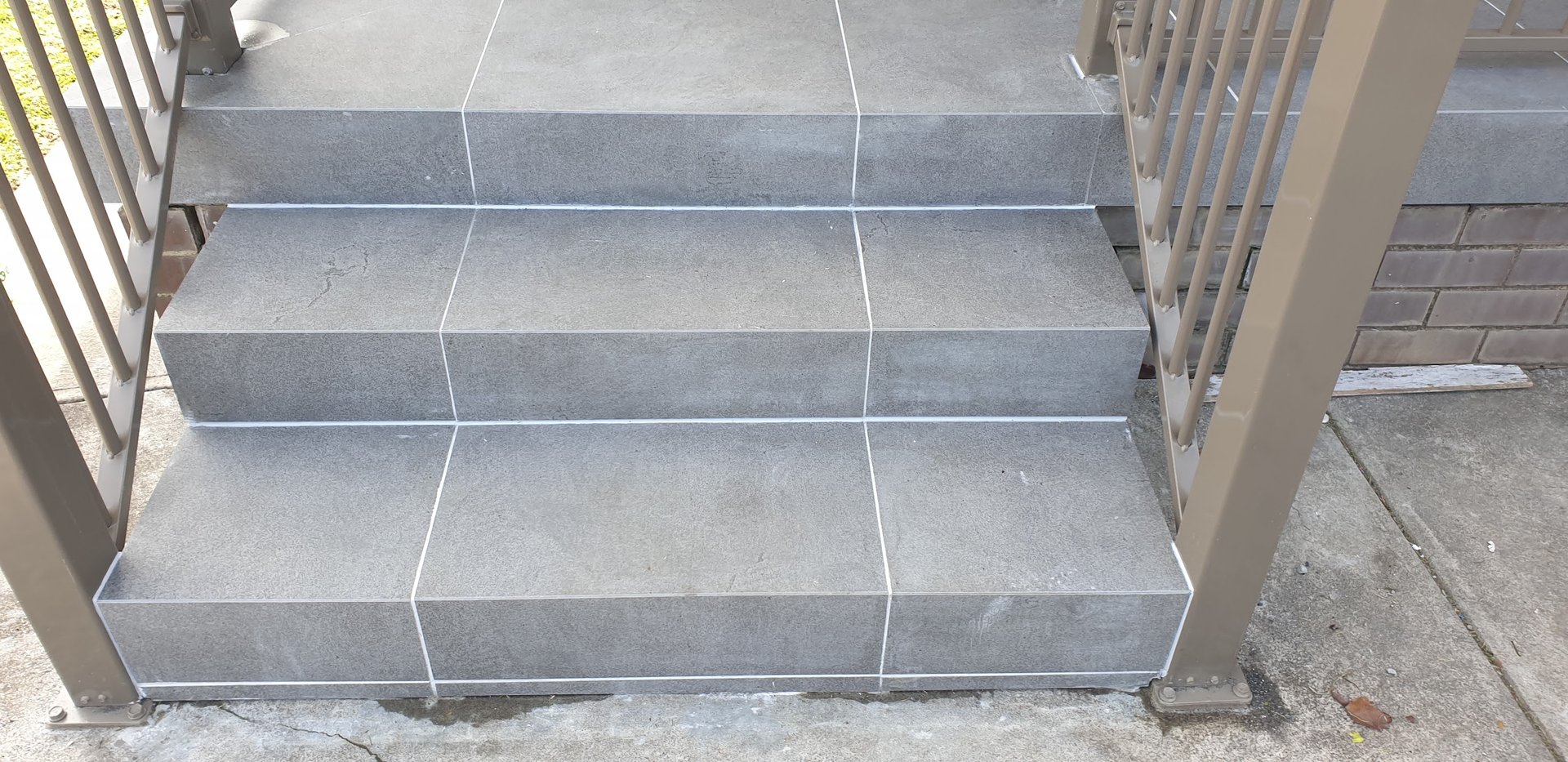Completed tiled entry steps with a metal handrail