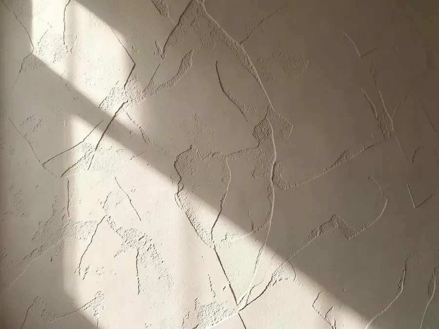 Textured decorative plaster wall in a soft beige tone lit from the side